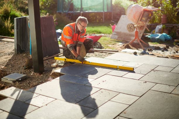 A construction worker leveling newly installed stone slabs for a patio A construction worker leveling newly installed stone slabs for a patio