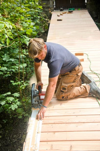 A contractor using a circular saw to cut wooden planks for a timber pathway installation A contractor using a circular saw to cut wooden planks for a timber pathway installation