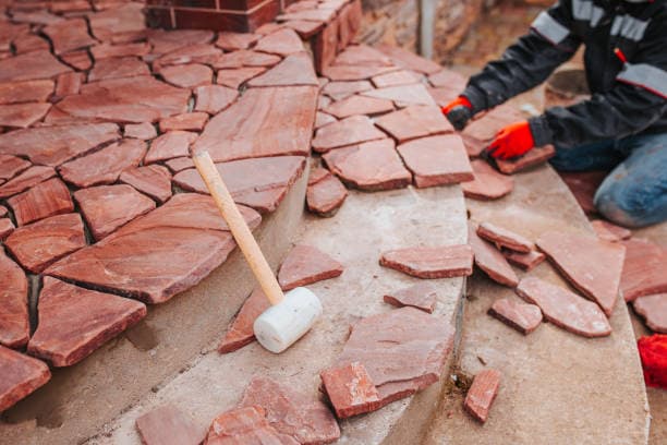 Worker installing irregular flagstone pieces on a patio or outdoor steps Worker installing irregular flagstone pieces on a patio or outdoor steps