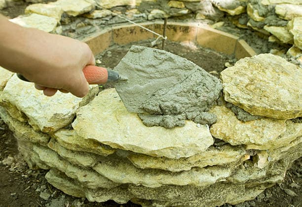 Close-up of a fire pit contractor applying mortar for a sturdy stone structure Close-up of a fire pit contractor applying mortar for a sturdy stone structure