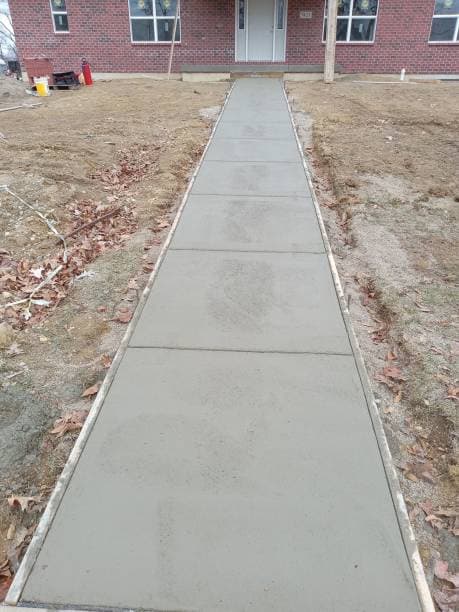 A newly installed concrete walkway leading to a brick building entrance A newly installed concrete walkway leading to a brick building entrance