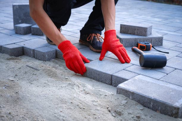Contractor placing bricks for a paver patio with essential tools nearby Contractor placing bricks for a paver patio with essential tools nearby