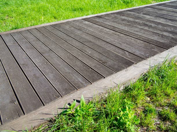 A completed wooden timber pathway with a clean, textured surface, bordered by grass A completed wooden timber pathway with a clean, textured surface, bordered by grass