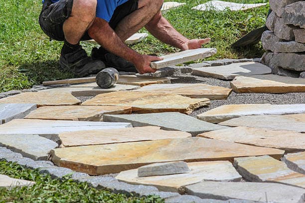 Worker installing flagstones on a patio, carefully placing each stone Worker installing flagstones on a patio, carefully placing each stone