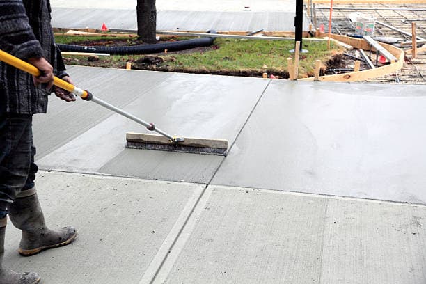 Worker smoothing freshly poured concrete for a new walkway Worker smoothing freshly poured concrete for a new walkway