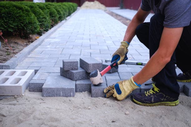 Worker laying paving stones for patio installation using a mallet Worker laying paving stones for patio installation using a mallet
