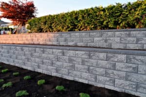 Gray stone retaining wall with greenery behind in a landscaped yard Gray stone retaining wall with greenery behind in a landscaped yard