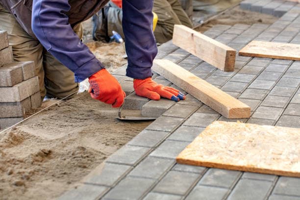 Worker installing patio pavers with precision for a durable outdoor surface Worker installing patio pavers with precision for a durable outdoor surface