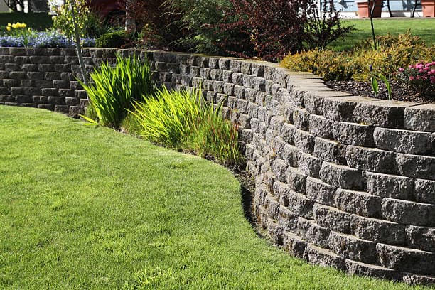 Curved stone retaining wall in landscaped yard with flowers and grass Curved stone retaining wall in landscaped yard with flowers and grass