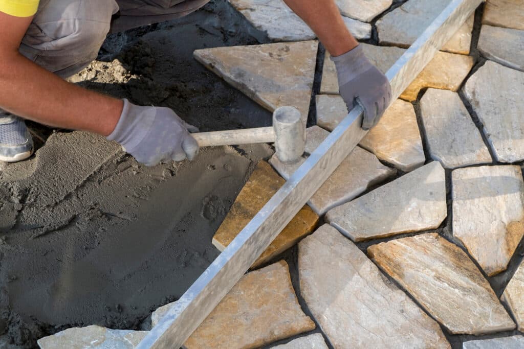 Worker laying stones with a hammer and level for hardscape installation Worker laying stones with a hammer and level for hardscape installation