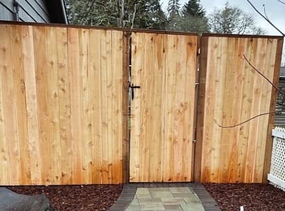 Newly built cedar privacy fence with a matching center gate, vertical pickets, top cap rail, and commercial-grade latch hardware