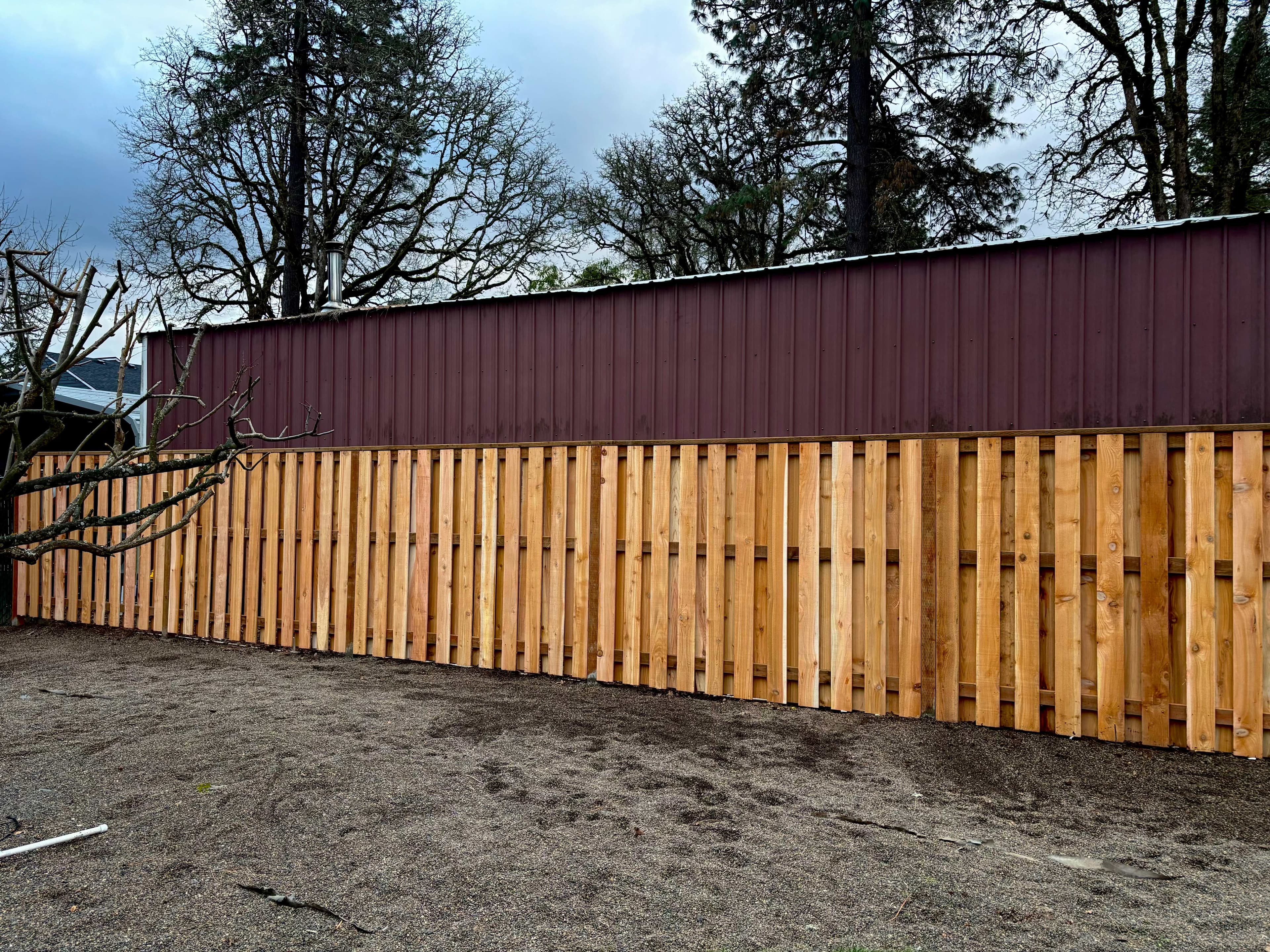 Long newly built cedar board-on-board privacy fence with vertical pickets running along an Oregon property line