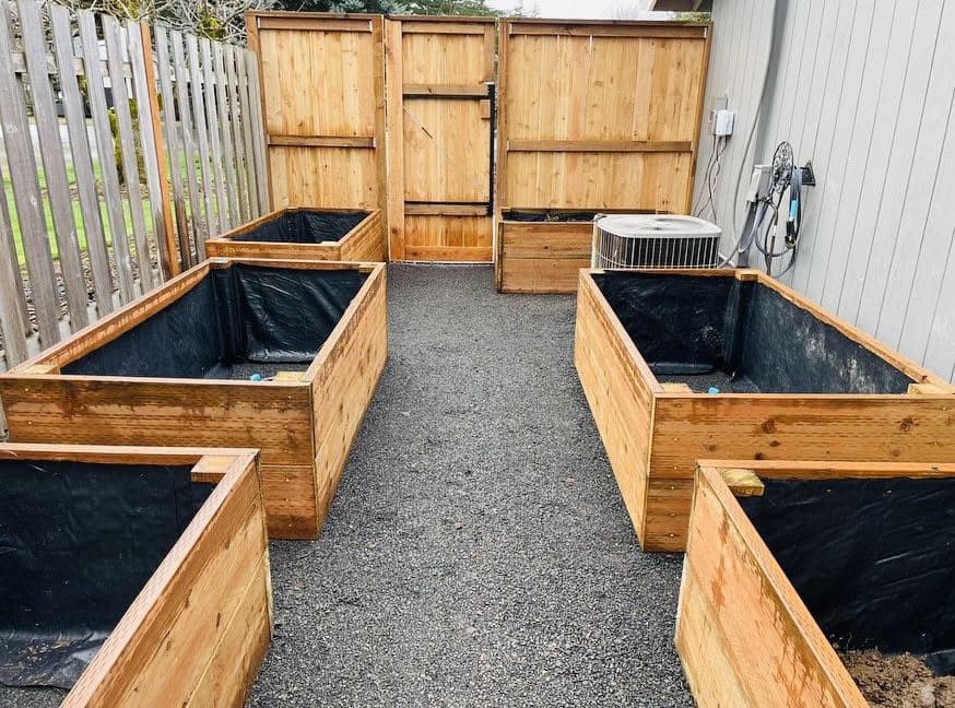 Custom cedar raised garden beds lined with landscape fabric arranged along a fresh gravel path in a fenced backyard