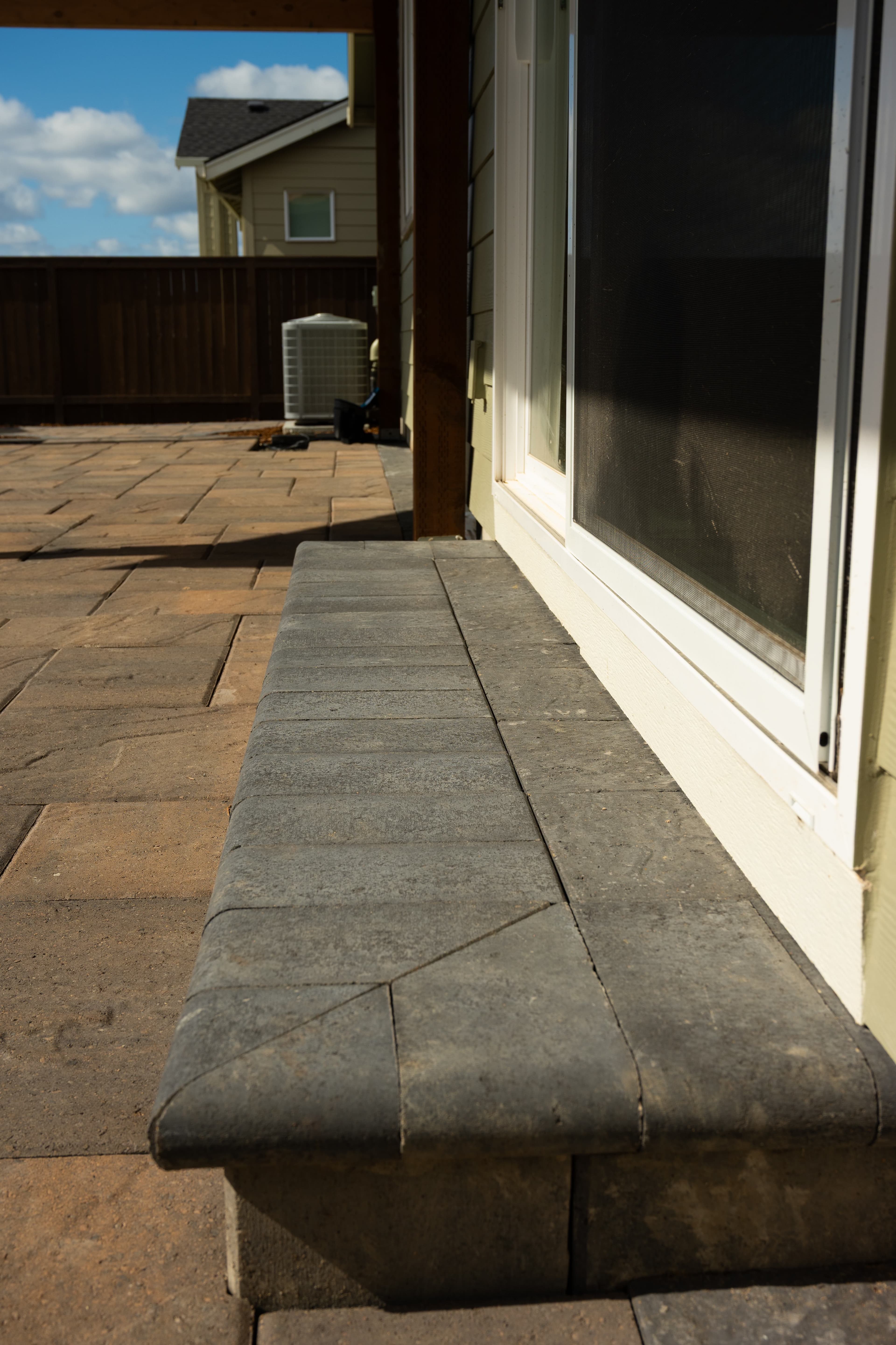 Low capped segmental-block seat wall with a smooth coping cap running along a paver patio beside a home's sliding door