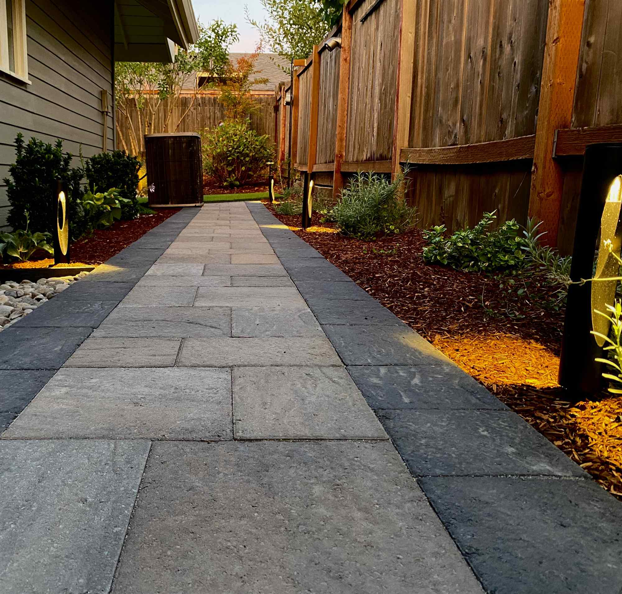 Path lights tracing a stone walkway through plantings after dark