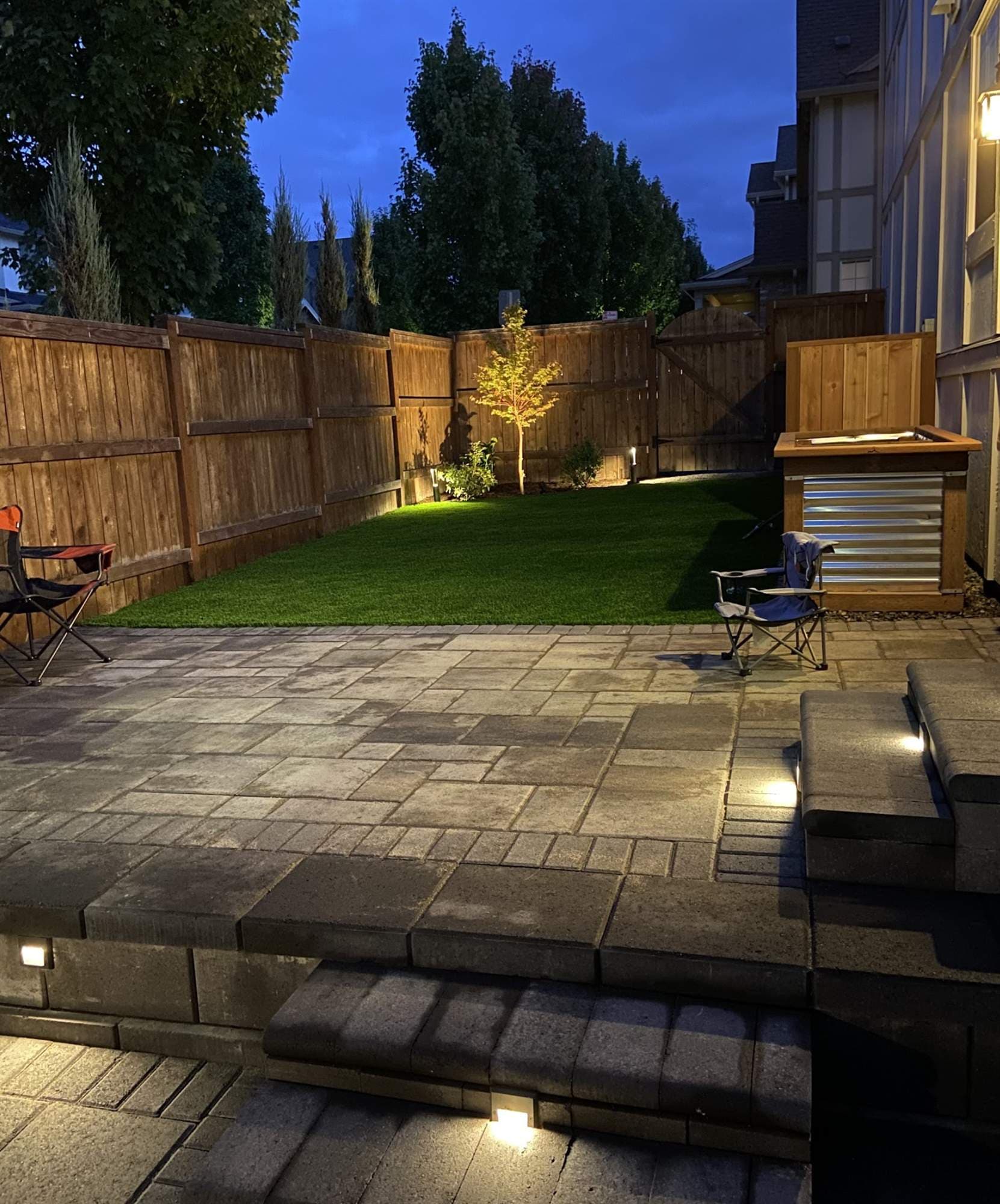 Low-voltage step and wall lighting glowing across a paver patio at dusk