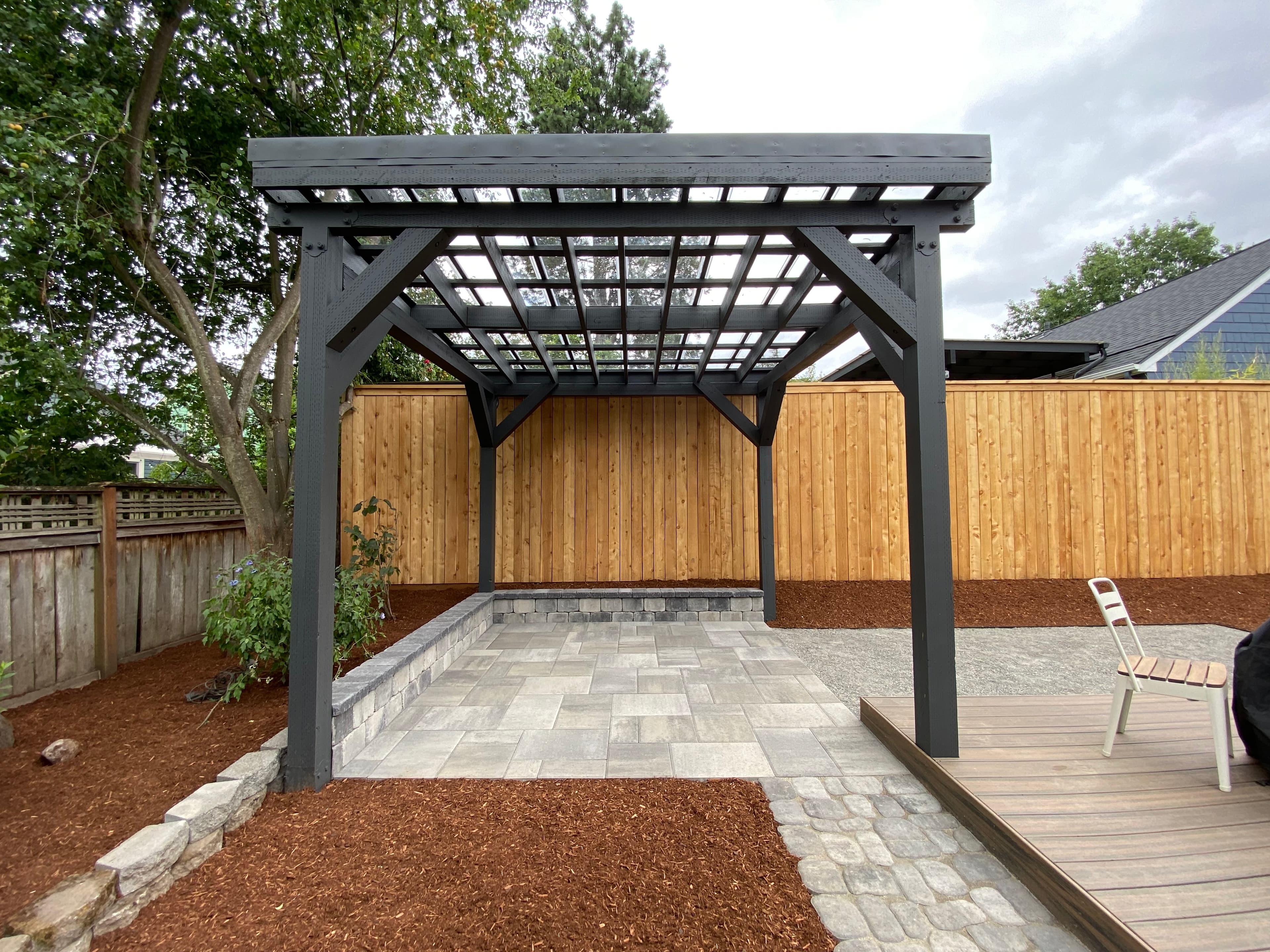 Freestanding dark-stained timber pergola with a clear lattice roof over a paver patio, framed by cedar privacy fencing