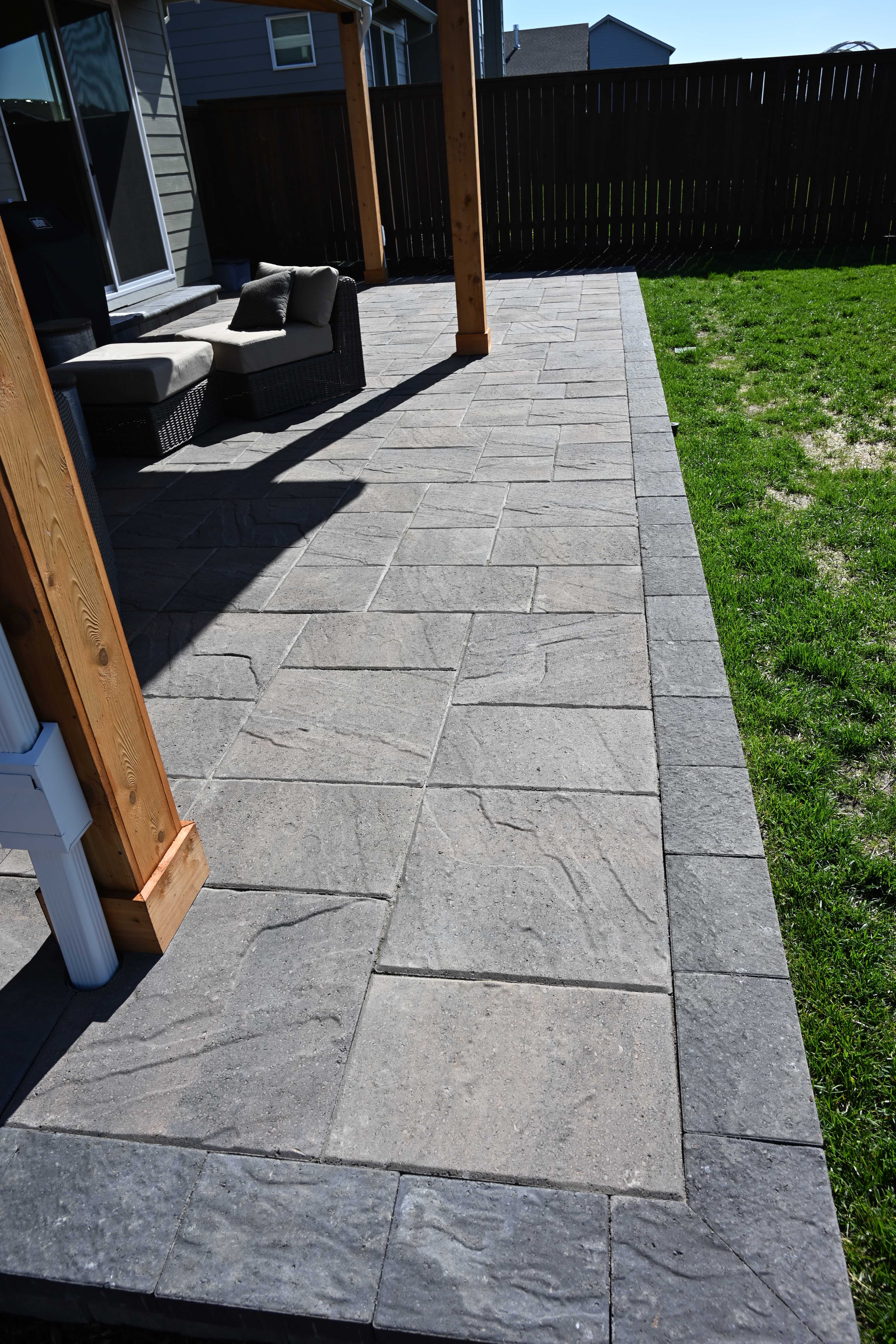 Cedar pergola posts set on a gray stone-textured paver patio casting long shadows alongside a home