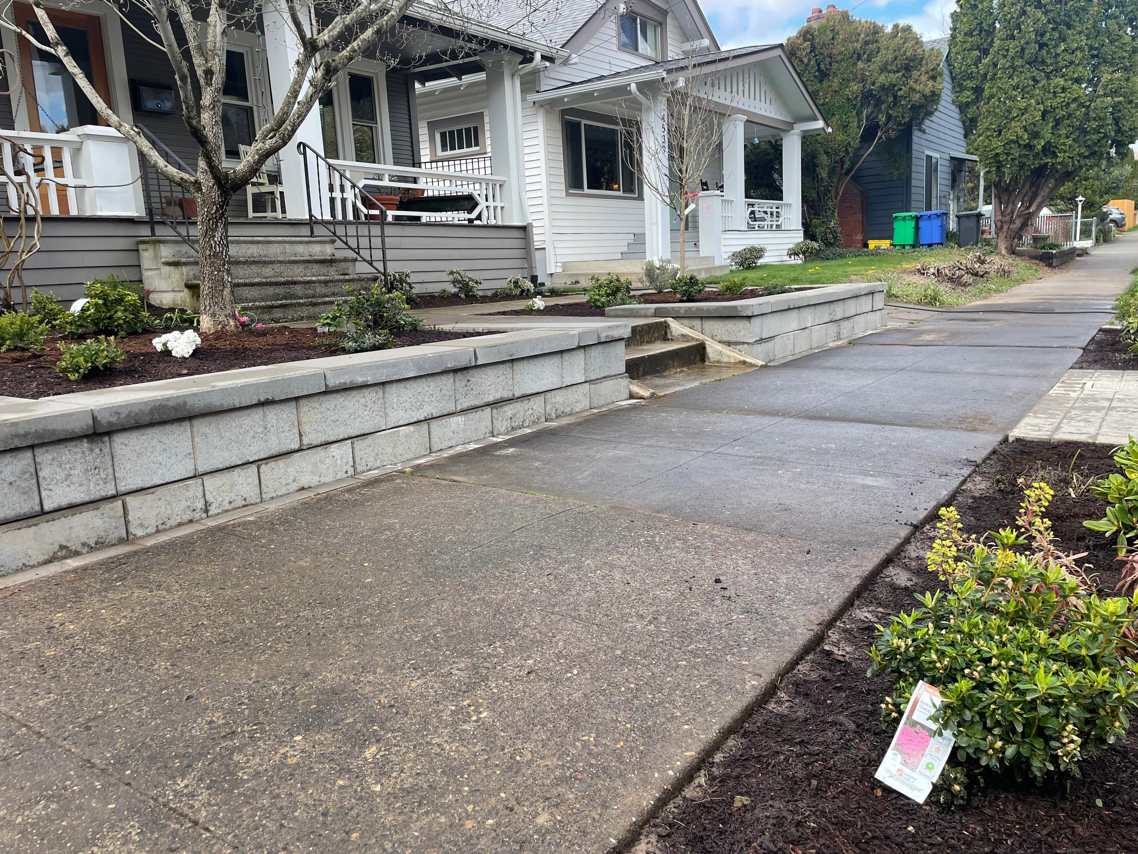 Low gray segmental-block retaining wall defining tiered planting beds along the frontage of a craftsman home
