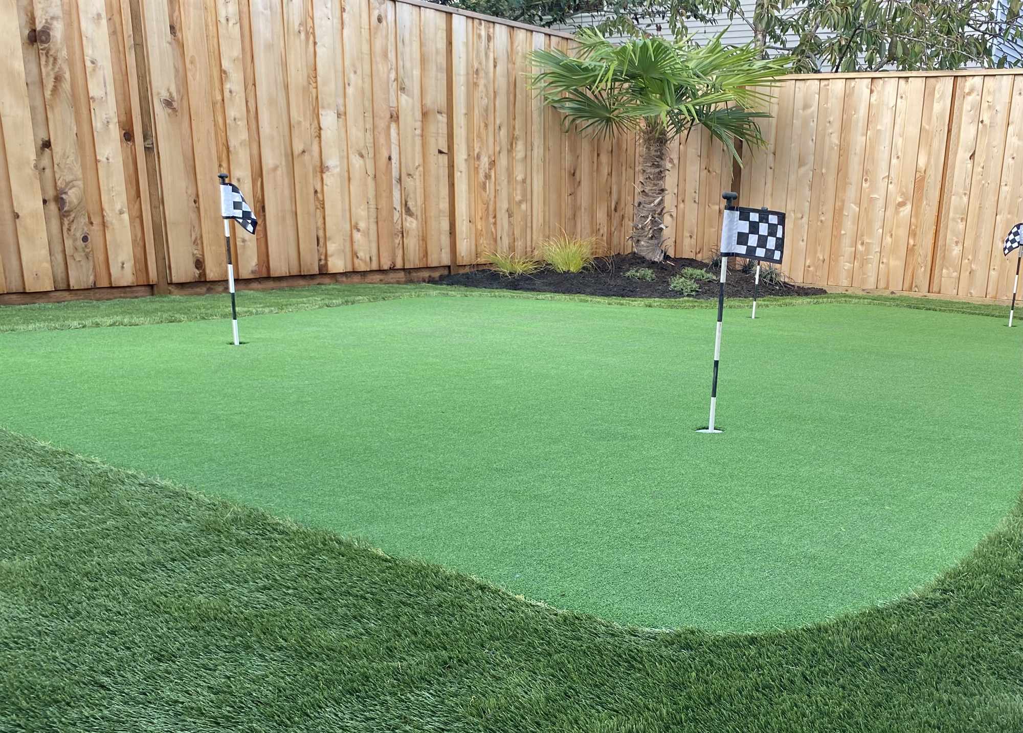 Backyard putting green tucked behind a cedar fence